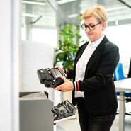 Frau überprüft eine Druckerpatrone vor einem geöffnetem Drucker